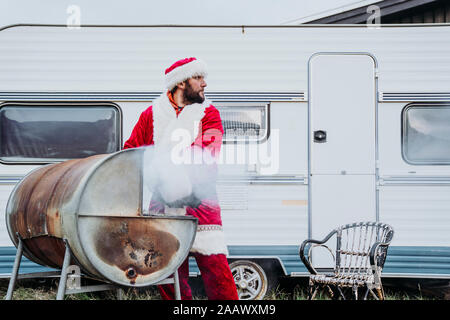 Le père Noël en train de préparer un barbecue en face d'un camping-car Banque D'Images