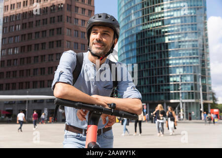 Smiling man with e-scooter sur city square, Berlin, Allemagne Banque D'Images