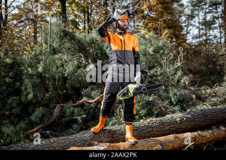 Portrait d'un bûcheron en vêtements de protection avec une tronçonneuse permanent sur les journaux dans la forêt Banque D'Images