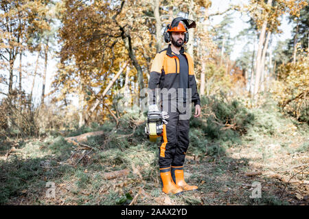 Portrait d'un bûcheron en vêtements de protection debout avec une tronçonneuse dans la forêt Banque D'Images