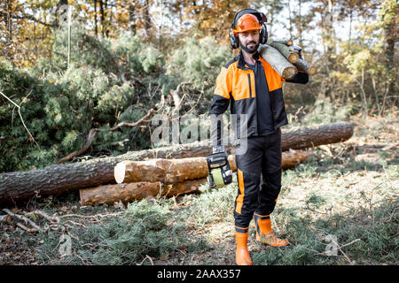 Portrait d'un marchand de vêtements de protection professionnelle en avec une tronçonneuse et en bois de sciage au cours des travaux sur l'exploitation forestière dans la forêt de pins Banque D'Images