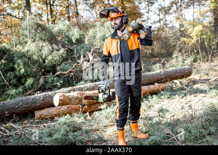 Portrait d'un marchand de vêtements de protection professionnelle en avec une tronçonneuse et en bois de sciage au cours des travaux sur l'exploitation forestière dans la forêt de pins Banque D'Images