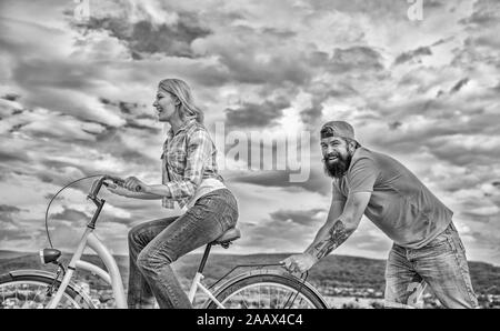 Des promenades en vélo femme fond de ciel. Pousser et la promotion. Impulsion à se déplacer. Homme pousse fille faire du vélo. Aide à croire en vous-même. Impulsion L'impression de commencer à bouger. Vélo fille tandis que l'homme la soutenir. Banque D'Images