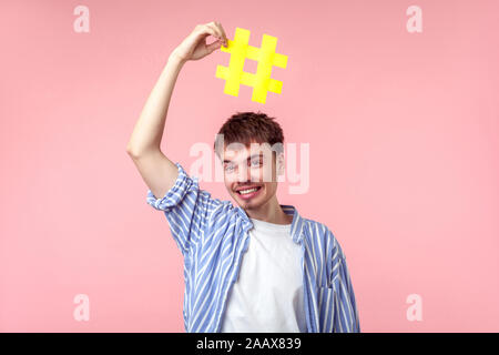 Portrait of happy blogger, drôle brown-haired man in casual shirt holding large big yellow hashtag signe au-dessus de sa tête et souriant avec excitation. Dans Banque D'Images