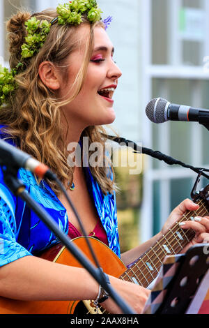 Maisy Beth, jeune chanteuse folk, chanter tout en jouant de la guitare acoustique dans la rue à Faversham Hop Festival. Porte guirlande de houblon. Banque D'Images