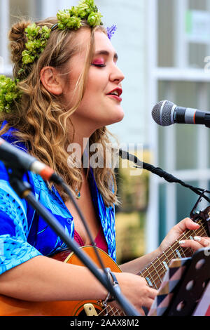 Maisy Beth, jeune chanteuse folk, chanter tout en jouant de la guitare acoustique dans la rue à Faversham Hop Festival. Porte guirlande de houblon. Banque D'Images