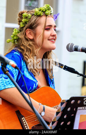 Maisy Beth, jeune chanteuse folk, chanter tout en jouant de la guitare acoustique dans la rue à Faversham Hop Festival. Porte guirlande de houblon. Banque D'Images