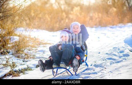 Les enfants jouent dans un parc d'hiver enneigé au coucher du soleil. La luge en bas de la colline et s'amusant. Les plaisirs de l'hiver. Jours fériés. Banque D'Images