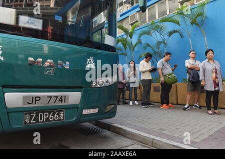 Un bus avec une plaque d'affectation chinois à côté de gens faisant la queue à un bureau de scrutin pour voter à l'élection du conseil de district Mong Kok. Hong Kong a tenu son conseil de district en vertu de l'élection une rare atmosphère de calme et de paix après des semaines d'intenses affrontements à de nombreuses universités entre manifestants anti-gouvernement et la police qui continue dans son sixième mois de manifestations. Hong Kong a tenu son conseil de district en vertu de l'élection une rare atmosphère de calme et de paix après des semaines d'intenses affrontements à de nombreuses universités entre manifestants anti-gouvernement et la police qui continuent en Banque D'Images