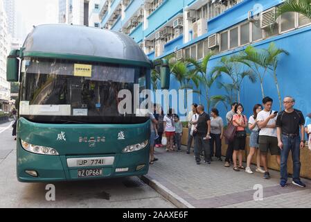 Un bus avec une plaque d'affectation chinois à côté de gens faisant la queue à un bureau de scrutin pour voter à l'élection du conseil de district Mong Kok. Hong Kong a tenu son conseil de district en vertu de l'élection une rare atmosphère de calme et de paix après des semaines d'intenses affrontements à de nombreuses universités entre manifestants anti-gouvernement et la police qui continue dans son sixième mois de manifestations. Banque D'Images