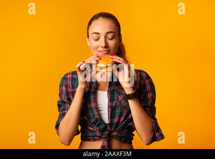 Girl Smelling Burger debout sur fond jaune Studio Banque D'Images