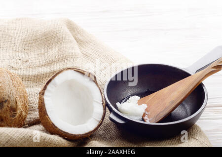 Coquille de noix de coco, avec de la viande, poêle en fonte et la spatule sur le chanvre sacs sur une table de cuisine en bois blanc Banque D'Images