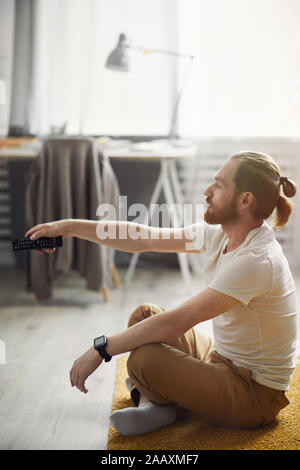 Vue de côté portrait de jeune homme moderne du passage d'une chaîne tout en regardant la TV à la maison assis sur marbre Banque D'Images
