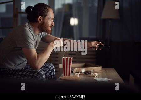 Vue de côté portrait de l'homme d'aujourd'hui de regarder la télévision dans le noir et les pop corn tout en appréciant les films de fin de nuit, copy space Banque D'Images