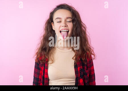 Portrait de l'adorable funny girl avec cheveux bouclés brunette in casual shirt debout avec les yeux fermé démontrant la langue, naughty chil désobéissant Banque D'Images