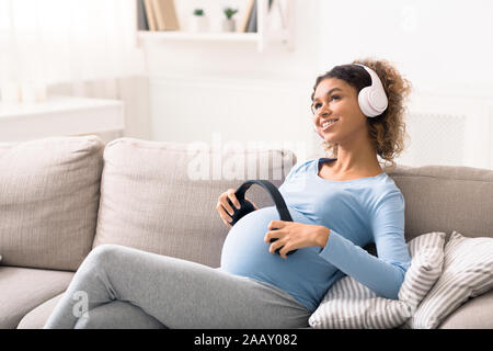 African-american pregnant woman listening to music in lving room Banque D'Images