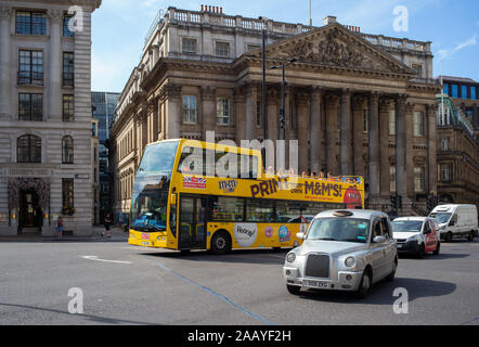 Un M&Ms parrainé tourist bus à toit ouvert classiques, via le quartier des banques de Londres à côté de la station de banque avec un taxi londonien d'argent. Banque D'Images