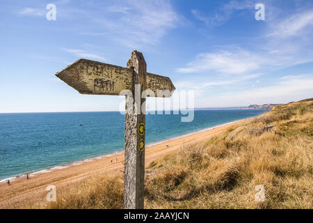 Un panneau en bois usés météorologiques montre la voie de l'ouest Dorset Coast Path le long de la section près de Burton Bradstock et montrant Chesil Beach et la côte Banque D'Images