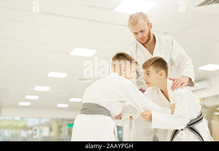 Deux garçons en kimono pratique technique avec leur entraîneur, debout près de l'enseignement et par eux au cours de la formation en salle de sport Banque D'Images