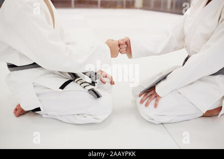 Close-up de deux garçons en kimono blanc assis sur le plancher et se serrer la main avant de lutte Banque D'Images