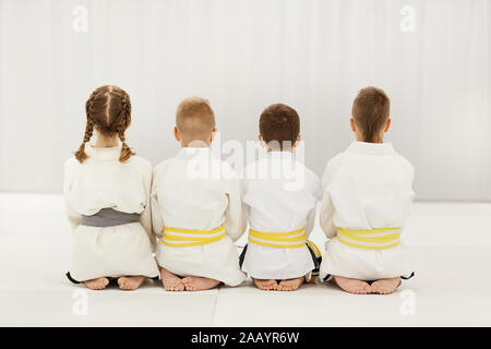 Vue arrière d'enfants pieds nus en kimono blanc assis sur le plancher ensemble dans une rangée Banque D'Images