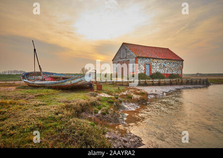 Vieux bateau de pêche traditionnel en bois près de la vieille Grange à charbon à Thornham Old Harbour sur la côte nord de Norfolk rétroéclairé par le soleil de soirée T5XJ8T Banque D'Images