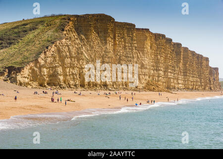 Les gens se détendre et bronzer sur la plage de Bridport, avec des falaises de grès stratifiés Bridport Dorset de l'ouest le long de la côte jurassique de Chesil avec b Banque D'Images