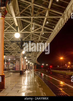 Nuit pluvieuse à la gare de York. Une plate-forme est éclairé par des lampes avec la lumière reflétée dans la surface humide. Un 19e siècle est couvert ci-dessus. Banque D'Images