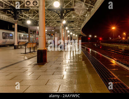 Nuit pluvieuse à la gare de York. Une plate-forme est éclairé par des lampes avec la lumière reflétée dans la surface humide. Un 19e siècle est couvert ci-dessus. Banque D'Images