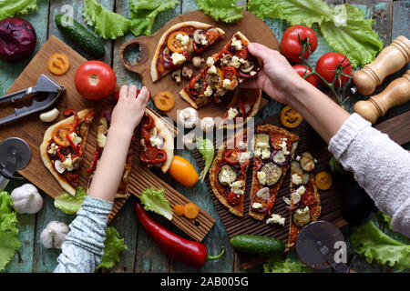 Maison végétarien cuisine de fête concept. Femme et enfant mains atteignant pour pizza avec champignons, poivrons, aubergines et le fromage de chèvre avec de la ve Banque D'Images