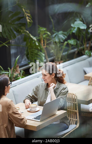 High angle portrait of two young women enjoying coffee sitting at table in outdoor cafe terrasse décorée avec des plats, copy space Banque D'Images