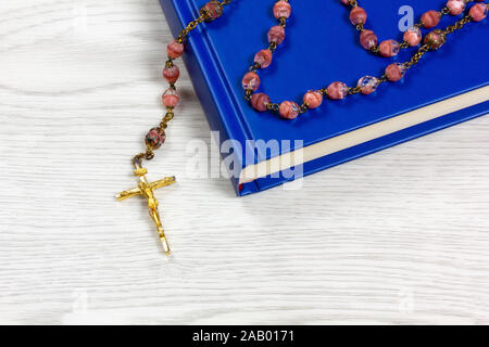 Chapelet avec des grains de couleur rose couché sur un livre sur une table en bois blanc Banque D'Images