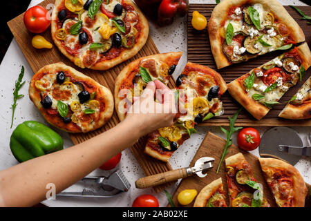 La femme de mettre les feuilles de basilic sur les pizzas. Des pizzas de style italien avec des olives, aubergines, poivrons, tomates et basilic sur fond blanc Banque D'Images