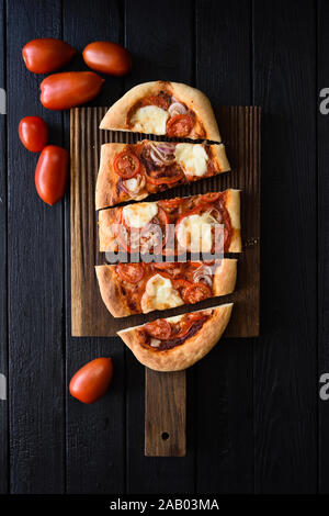 Pizza végétarienne rustique. Pizza ovale fraîchement cuits au four avec légumes servi avec des tomates crues sur fond noir top view copy space Banque D'Images