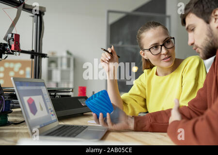 Les jeunes femmes confiant de parler à son collègue concepteur avec l'objet en plastique bleu imprimé sur la machine d'impression 3D Banque D'Images