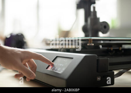 Main de jeune designer appuyer sur la touche du panneau de commande de l'imprimante 3d en allant d'imprimer les nouveaux points in office Banque D'Images