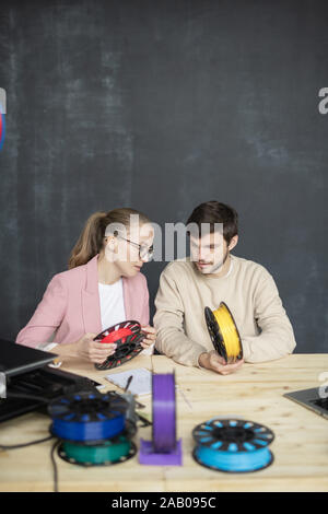 Deux jeunes designers créatifs avec des bobines de filaments de couleurs diverses assis par table au cours de la discussion de travail Banque D'Images