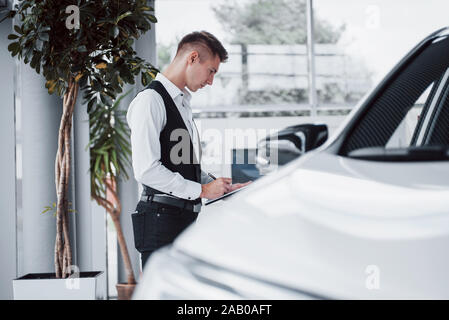 Jeune homme debout dans la salle d'exposition à des voitures Banque D'Images