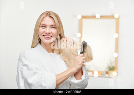 Heureux et en santé, jeune femme avec le sourire à pleines dents brosser ses longs cheveux blonds Banque D'Images