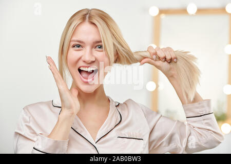 Fille excité en pyjama beige avec de longs cheveux blonds épais en bonne santé Banque D'Images