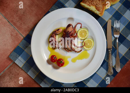 Une plaque de cuisson petit polype et citrons garnis dans l'huile d'olive sur une table en céramique avec de vieux couverts photographié d'en haut Banque D'Images