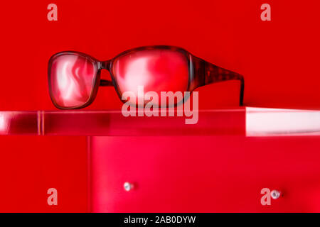 Verres sur un écran en plexiglas sur fond rouge Banque D'Images