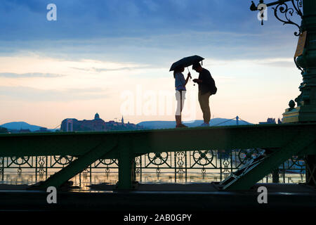 Silhouette de jeune couple debout sur un pont poutre avec caméra et ombrelle Banque D'Images