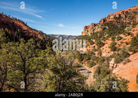 Sur une étroite route sinueuse, un SUV d'argent les périphériques à des forêts vert avec orange et red rock cliffs et hoodoo des tours dans le désert du sud de l'Utah. Banque D'Images