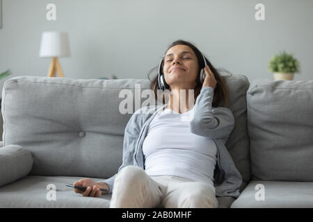 Lean Relaxed woman on couch écouter chanson favorite à travers des écouteurs Banque D'Images