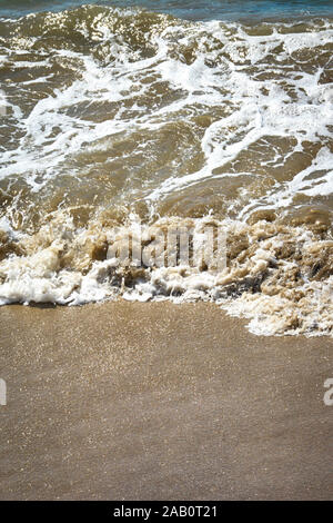 Vue rapprochée de l'eau de couleur brun faire de petites vagues se brisant sur la plage avec texture sableux grossier Banque D'Images