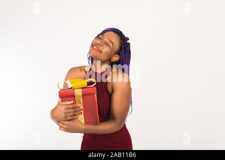 Une fille à la peau sombre est titulaire d'un énorme cadeau rouge avec un arc d'or dans ses mains, regarde la caméra et sourit. Concept de maison de vacances, Nouvel an et de noël, re Banque D'Images