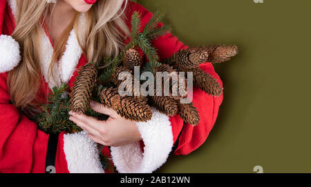 Noël et Nouvel An vacances d'arrière-plan. Une jeune fille dans un costume de Père Noël tient dans ses mains un bouquet de branches de sapin avec les cônes. Christma Banque D'Images