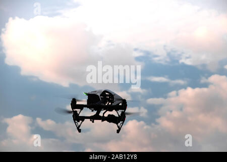 Un quadrocopter noir avec un appareil photo numérique vole dans un ciel nuageux. Des drones drone avec hélices sur fond de nuages rose et bleu s Banque D'Images