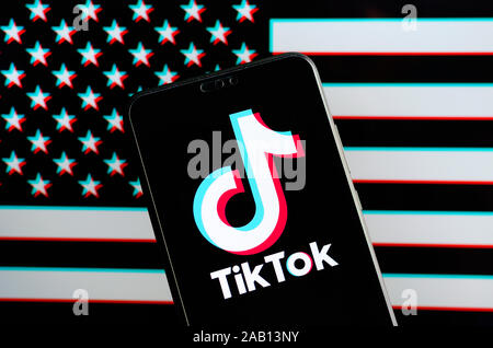 TikTok logo app sur le smartphone et un drapeau américain avec split-RVB effet sur l'écran de l'ordinateur portable derrière elle. Concept fort photo. Banque D'Images
